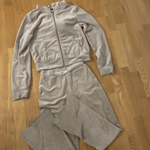 Beige velourset från Gina Tricot - Säljer ett mysigt beige velourset från Gina Tricot. Setet består av en långärmad tröja med dragkedja och matchande byxor. Perfekt för en avslappnad dag hemma eller en stilren look på stan. Tröjan har en bekväm passform och byxorna har fickor baktill.