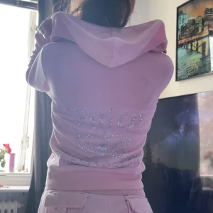 Rosa hoodie från Juicy Couture - Säljer en rosa hoodie från Juicy Couture med glittrande stenar på ryggen som bildar texten 'Juicy Couture' och en krona. Hoodien har dragkedja och långa ärmar, perfekt för en avslappnad stil. Den är både snygg och bekväm!