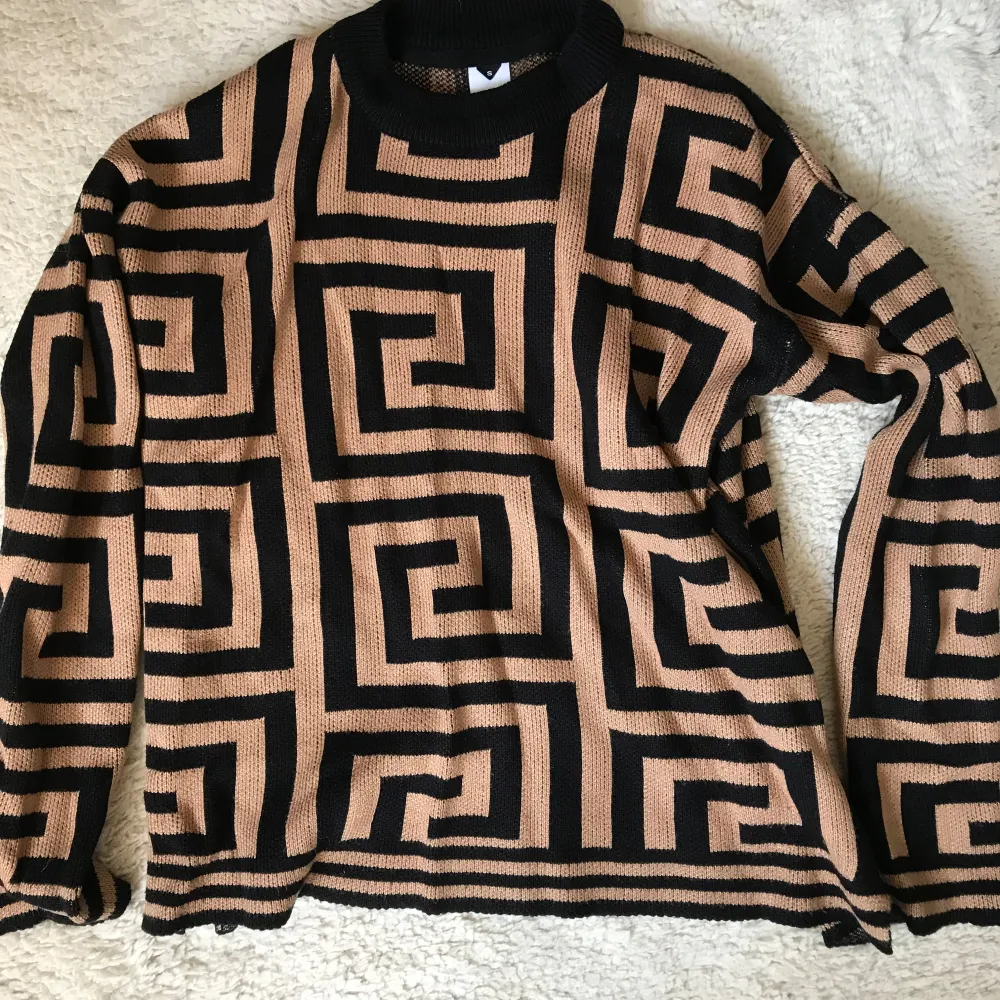 Säljer en unik svart och beige tröja från Visual Clothing Project med ett geometriskt mönster. Tröjan har långa ärmar och en rund halsringning. Perfekt för att sticka ut i mängden!. Neuletakit & Villapaidat.