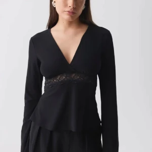 Svart långärmad topp med spetsdetalj - fin svart topp med v-ringning och spetsdetalj. Toppen har långa ärmar och fin passform som ger en stilren look.  den e från gina. använd en gång