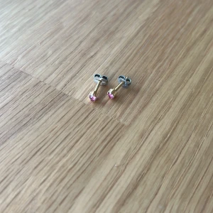 Guldörhängen med rosa stenar - Snygga små och diskreta guldörhängen med glittrande rosa stenar. Säljer då jag har dubbla uppsättningar. Tyvärr finns inte orginalplupparna så därför är de missmatchande, men detta påverkar inte användningen. Örhängena är noga tvättade och disinfekterade. Märket är okänt.