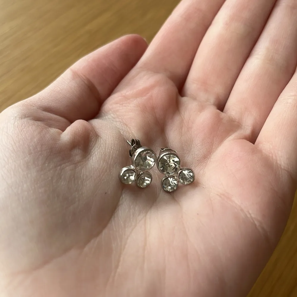 Snygga silver örhängen med tre glittrande stenar i varje. Diskreta men ändå iögonfallande då de gnistrar extra mycket i solen. Säljer då jag inte använder silver. Tyvärr finns inte orginalplupparna så därför är de missmatchande, men detta påverkar inte användningen. Örhängena är noga tvättade och disinfekterade. Märket är okänt.. Asusteet.