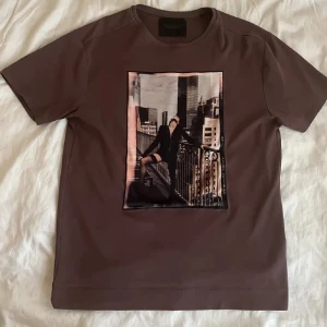 Vinröd/brun Limitato t-shirt med tryck - Snygg  t-shirt från Limitato med ett stort tryck av en stadssilhuett och en person på framsidan. T-shirten har en rund hals och korta ärmar, perfekt för en trendig look. Nypris 3000kr, mitt pris endast  699kr! köpt från NK. 