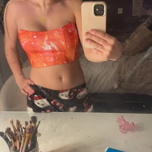 Orange mönstrad tubtopp - Säljer en snygg orange tubtopp med ett unikt mönster i vitt och rosa. Toppen är axelbandslös och har en tight passform, perfekt för sommarens varma dagar. Materialet är mjukt och bekvämt.