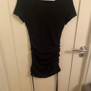 Svart ribbad klänning från Shein - Snygg svart ribbad klänning från Shein med korta ärmar och justerbar snörning i sidorna. Perfekt för en stilren look med en touch av elegans. Klänningen har en tight passform som framhäver figuren.