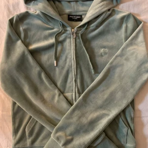 Grön hoodie från Juicy Couture - Mysig mintgrön hoodie från Juicy Couture. Den har en dragkedja framtill och en praktisk huva med snören. Som ni ser på bild 2 så e den ena metall biten tyvärr sönder på ena snöret därav priset. Nypris 1200.