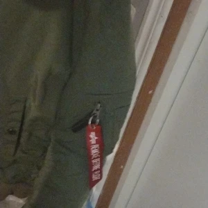 Grön Orginal bomberjacka från Alpha Industries(första utgåva)! - Säljer en grön  bomberjacka från Alpha Industries i bra skick. Den har en klassisk orange insida och en cool röd tagg med texten 'Remove Before Flight'. Perfekt för höst och vår, med dragkedja och fickor för extra stil och funktionalitet. Sitter som klistrad. Som de ska vara :) Ledsen för stressbilder men kan skicka vid interesse . Nypriset på denna är oviktigt igentligen med tanke på att det är orginalutgåvan gör att de inte är vilken alpha som helst. Men nypriset va på 2200 Nyskick mvh