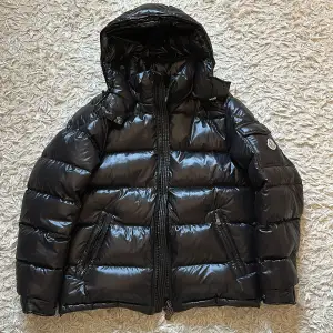 Säljer en helt ny, aldrig använd Moncler Maya jacka i storlek 2. Den svarta jackan är fylld med dun och erbjuder både stil och funktion med vattentåligt material, perfekt för kalla vinterdagar. Jackan kommer med autenticitetsbevis,  extra knappar och allt originellt innehåll, vilket garanterar äkthet och nyskick. Den klassiska designen och Monclers ikoniska logotyp gör den till en tidlös investering, och är helt perfekt för vintern. NFC funkar såklart. Hör av dig vid minsta intresse!