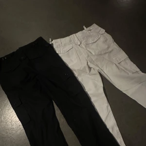 Svarta och vita cargobyxor - Två par cargobyxor i svart och vitt. De har flera praktiska fickor med knappar och en loose passform. Inte använt många gånger, går även att köpa ett par! Byxorna är i ett jätte bra skick och redo för nya ägare! Köpta från weekday!  500kr för båda, 300kr för ett par!