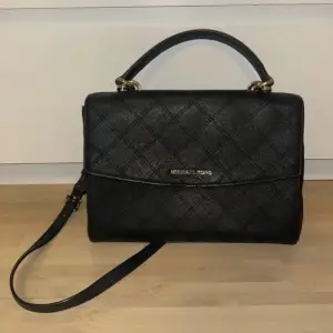 Snygg svart handväska från Michael Kors i quiltat mönster. Väskan har både handtag och en avtagbar axelrem för flexibilitet. Den är i mycket bra skick och har en praktisk dragkedja inuti. Perfekt för både vardag och fest!