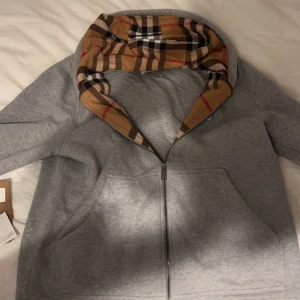  Burberry hoodie - Säljer en snygg grå hoodie från Burberry med deras ikoniska mönster i luvan. Perfekt för höst och vår, med en stilren design och bekväm passform. Den har en broderad logga på bröstet och är i mycket bra skick. Passar både till vardags och lite finare tillfällen. Självklart äkta och har dessutom kvar tags! Hör av er om ni har några frågor ✌🏻