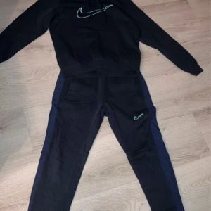 Svart hoodie från Nike - Säljer en svart dress från Nike i mycket bra skick. Den har en stor Nike-logga på bröstet och är perfekt för både träning och vardag. Materialet är mjukt och bekvämt, och den har långa ärmar. Passar perfekt för höst och vinter!