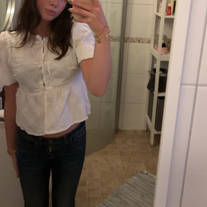Vit blus med spetsdetaljer - Säljer en söt vit blus med korta ärmar och fina spetsdetaljer. Blusen har en knytning framtill och en lätt volang vid midjan. Perfekt för alla tillfällen! 🌸