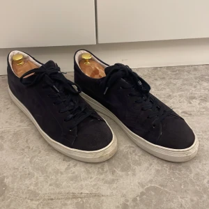 Mörkblåa Mocka sneakers från Björn Borg - Säljer ett par mörkblåa mocka sneakers från Björn Borg i bra skick. De har en stilren design med snörning och en vit sula som ger en snygg kontrast. Perfekta för både vardag och festliga tillfällen. Storlek 44.
