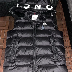 Svart dunväst från Moncler - Säljer en snygg svart dunväst från ”Moncler” i mycket bra skick. Västen har en dragkedja framtill och två praktiska fickor med dragkedjor. Perfekt för höst och vinter, och den har en cool logga på bröstet. Passar både till vardags och festliga tillfällen.