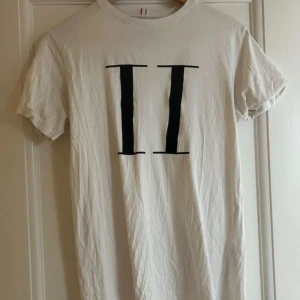 Vit t-shirt från Les Deux - Säljer en stilren vit t-shirt från Les Deux i storlek XS. Den har ett stort svart tryck med romerska siffror 'II' på framsidan. Perfekt för en casual look och passar till både vardag och fest. T-shirten är i bra skick och gjord av mjuk bomull.