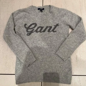Grå tröja från Gant - Säljer en snygg och stilren grå tröja från Gant i mycket bra skick. Den har ett klassiskt Gant-tryck på framsidan och är perfekt för både höst och vinter. Tröjan är långärmad och gjord av 100% lammull, material som håller dig varm. Perfekt för vardagsbruk eller en avslappnad dag ute. Storlek ca men motsvarar 134