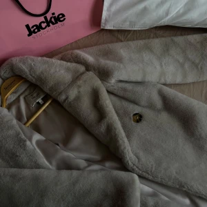 Beige pälsjacka från Dry Lake lång modell - Säljer en supermjuk och stilren grå pälsjacka från Dry Lake i storlek XS. Jackan har en elegant design med en knapp framtill och är perfekt för kyliga höst- och vinterdagar. Den är i mycket bra skick och ger en lyxig känsla. Perfekt för att hålla sig varm och snygg!