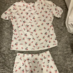 Blommigt pyjamas set - Säljer ett vitt pyjamas set med blommönster. De är gjorda i mjuk bomull och har en elastisk midja för extra komfort. Observera att det finns en liten foundation fläck på shortsen, men det går nog lätt ut i tvätten. Passar bra till avslappnade tillfällen eller som mysplagg hemma. Jätte mysigt tyg och perfekt att sova i . Tror den är i stl M, och kommer inte ihåg vart jag köpte den ifrån. Använd några gånger.