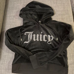 Svart velour hoodie från Juicy Couture - Säljer en supermjuk och snygg svart velour hoodie från Juicy Couture. Den har långa ärmar och en stor luva, perfekt för mysiga dagar. Framsidan pryds av texten 'Juicy' i glittrande stenar. Perfekt för att ge din outfit en touch av glamour! ✨