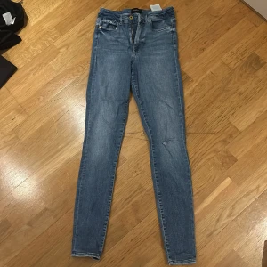 Blå jeans från Vero Moda - Säljer ett par snygga blå jeans från Vero Moda i storlek S/32. De har en tight passform och är tillverkade i denim. Jeansen har en slitning på ena benet. Perfekta för både vardag och fest!