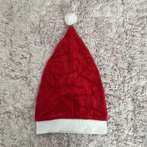 Röd tomteluva med vit kant - Säljer en klassisk röd tomteluva med vit kant och en fluffig vit boll på toppen. Perfekt för julfirandet och att sprida lite extra julstämning. Luvan är mjuk och bekväm att ha på sig hela dagen. Passar de flesta huvudstorlekar. 🎅✨