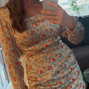 Blommig långärmad klänning - Säljer en superfin blommig klänning med långa ärmar. Perfekt för vår och sommar! Den har en tight passform som framhäver figuren och ett färgglatt mönster med röda och gröna blommor. Materialet känns mjukt och bekvämt mot huden.
