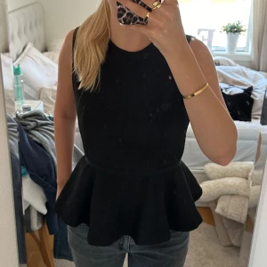Svart ärmlös topp från H&M - Säljer en snygg svart ärmlös topp från H&M. Den har en peplum-stil som ger en fin siluett och är perfekt för både vardag och fest. Toppen är i storlek M och har en dragkedja i ryggen för enkel påklädning. Materialet känns bekvämt och passar bra till jeans eller kjol.