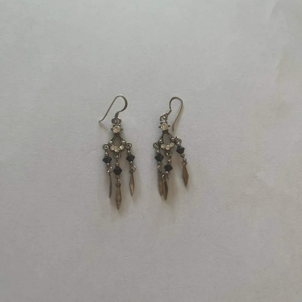 Säljer ett par snygga silvriga örhängen gjorda av äkta silver med svarta pärlor och hängande detaljer. De har en elegant design med små glittrande stenar och droppformade hängen. Perfekta för en festlig kväll eller en speciell tillställning!💕. Asusteet.