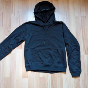 CP company hoodie - En svart CP Company hoodie  Strl M  Cond 6/10 den har ett litet hål i högra armhålan. Men det går lätt att sy ihop. 