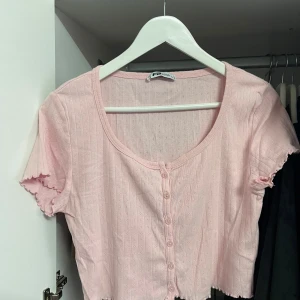 Rosa kortärmad topp från FB Sister - Säljer en söt rosa topp från FB Sister. Den är kortärmad och har små knappar framtill. Storlek L, passar M. Toppen är croppad och har en fin ribbad struktur med små hålmönster. Perfekt för sommardagar eller en avslappnad vårlook! 