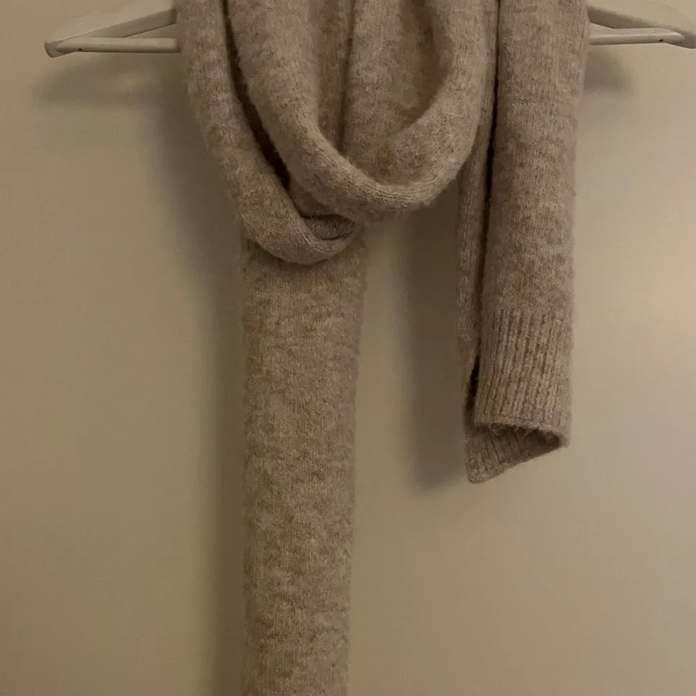 Säljer en supermysig beige stickad halsduk som är perfekt för kyliga dagar. Den är riktigt mjuk och varm, vilket gör den idealisk för höst och vinter. Halsduken har en enkel och stilren design som passar till det mesta i garderoben. Perfekt för att hålla stilen och värmen samtidigt!. Muu.