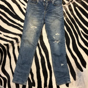 Blå jeans från Zara - Säljer ett par snygga blå jeans från Zara. De har en cool slitning på framsidan som ger dem en trendig look. Jeansen är i en klassisk blå färg och har en normal passform. Perfekta för vardag!