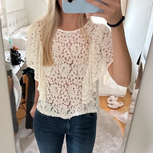 Vit spetsblus från Gina Tricot - Säljer en superfin vit spetsblus från Gina Tricot. Blusen har korta ärmar och ett vackert blommigt spetsmönster. Perfekt för sommarens fester eller en dag på stan. Den har en liten knapp i nacken för enkel på- och avtagning. Passar mig med storlek S!