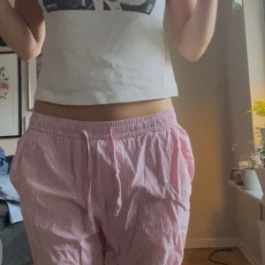 Rosa randiga byxor - Säljer ett par supermysiga rosa randiga byxor. De är loose fit och perfekta för en chill dag hemma eller en avslappnad promenad. Byxorna har en bekväm resår i midjan och är gjorda i ett mjukt material som känns skönt mot huden.