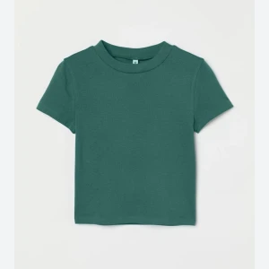 Grön kortärmad topp - Säljer en snygg grön kortärmad topp i bomull. Den är perfekt för vardagsbruk och har en enkel, stilren design. Toppen är i bra skick och passar perfekt till jeans eller kjol. 💚