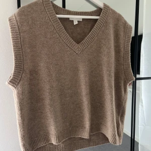 Beige stickad väst - Säljer en supermysig beige stickad väst med v-ringning. Perfekt för lager-på-lager under hösten eller vintern. Den har en lite oversized passform och ribbade kanter som ger en snygg finish.
