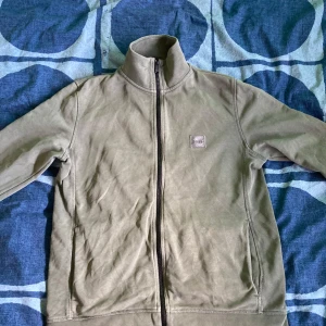 Grön fleecetröja från Boss - Säljer en snygg mörkgrön zip-up fleece från Hugo Boss. Den har en dragkedja där det står Boss på och en liten logga på bröstet. Perfekt för kyliga dagar och passar bra med jeans. Tröjan är i bra skick och stilig! 