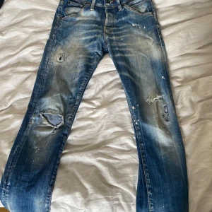 Blå jeans från Jack & Jones - Säljer ett par snygga blå jeans från Jack & Jones. De har en cool slitning och lite färgstänk för en avslappnad look. Modellen är slim fit och heter Glenn. Perfekta för en casual stil! 29 W 30 L