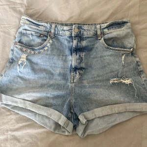 Jeansshorts från H&M - Säljer ett par snygga jeansshorts från H&M i storlek XL. De är högmidjade och har en cool, sliten look med broderade detaljer och ett liten bi på bakfickan. Perfekta för sommaren!