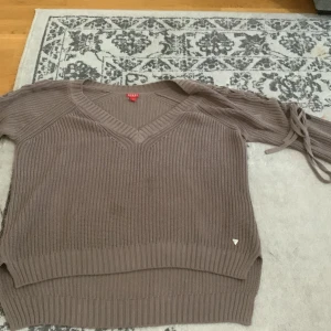 Beige stickad tröja med knytband - Säljer en superfin beige stickad tröja med v-ringning och långa ärmar. Tröjan har snygga knytband vid ärmsluten och ribbade detaljer vid nederkanten. Perfekt för höst och vinter!