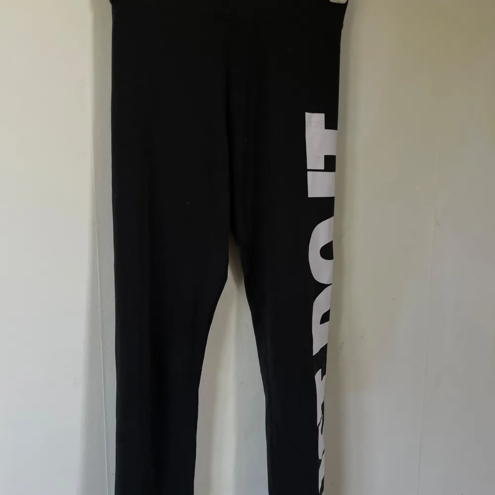 Säljer ett par svarta leggings från Nike med det ikoniska 'Just Do It' trycket i vitt längs benet. Perfekta för träning eller en avslappnad dag. De är i bra skick och superbekväma!. Sportswear.