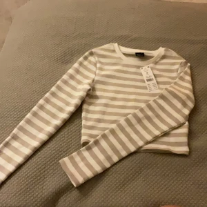 Randig tröja  - En jättefin beige och vit randig tröja ifrån Gina tricot, nytt skick och aldrig använd med prislappen kvar. Tight och lite croppad med långa ärmar. Slutsåld på hemsidan för 229 kr. 