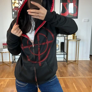 Svart hoodie med rött mönster💞 - Säljer en cool svart hoodie med ett stort rött mönster på framsidan. Den har en dragkedja och en stor huva med vit text. Perfekt för en avslappnad stil och passar bra till jeans. Huvan har en röd insida som matchar det röda mönstret. Superbekväm och perfekt för höst och vinter!
