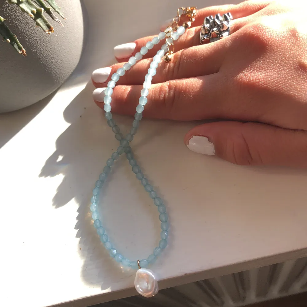 Säljer ett superfint halsband med ljusblå pärlor och en stor vit pärldetalj som hänge. Halsbandet har en guldig kedja som ger en lyxig touch. Perfekt för både vardag och fest!. Accessoarer.