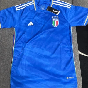 Blå fotbollströja från Adidas - Säljer en snygg blå fotbollströja från Adidas med Italiens landslagsemblem på bröstet. Tröjan har korta ärmar och klassiska vita Adidas-ränder på axlarna. Perfekt för fotbollsfans som vill visa sitt stöd för Italien! 💙