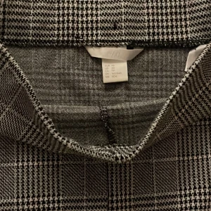 Rutig kjol från H&M - Snygg rutig kjol från H&M i svart och grått. Kjolen har en klassisk passform och är perfekt för både kontoret och vardagsbruk. Den är gjord i ett bekvämt material som känns skönt mot huden. Ett måste i garderoben för en stilren look!