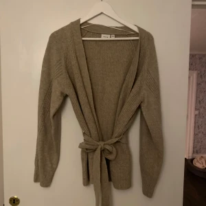 Beige stickad kofta från VILA - Mysig beige stickad kofta från VILA i storlek M. Den har långa ärmar och ett knytband i midjan för en fin passform. Perfekt för höst och vinter när du vill hålla dig varm och stilren. 🧥✨