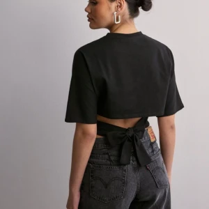 Open back tie tee - Ny med prislapp Snygg svart topp med korta ärmar och en unik knytning i ryggen. Perfekt för en stilren och modern look. Passar både till vardags och festliga tillfällen.