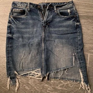 Nedsliten Jeanskjol  - Nedsliten jeanskjol med frasande kanter som är en trendig look. Den är typ marinblå med ljus tvätt i mitten. Framhäver dessutom kurvorna 👌